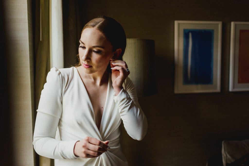 Bride next to window putting on her earrings