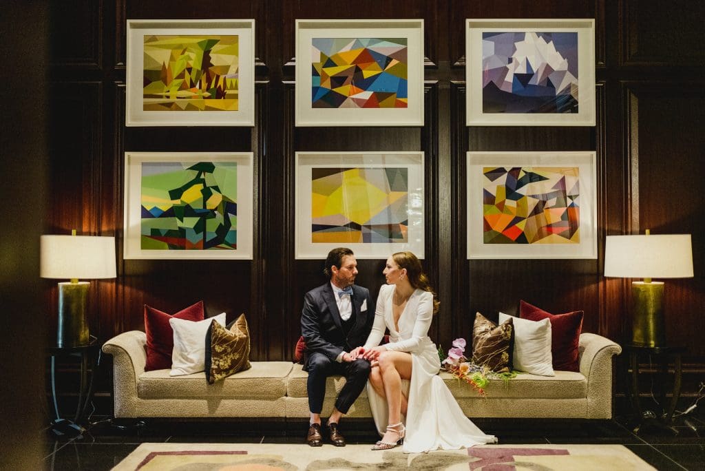 Bride and groom sitting together on a long chair, gazing lovingly into each other’s eyes.
