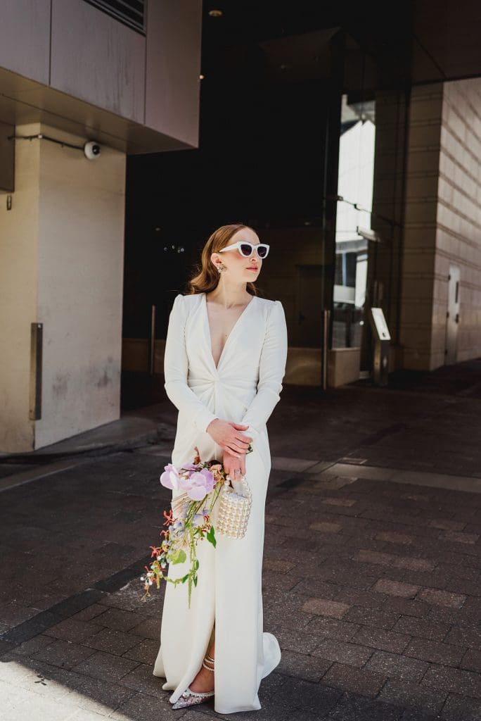 Bride wearing sunglasses, holding a bouquet, and looking off into the distance.