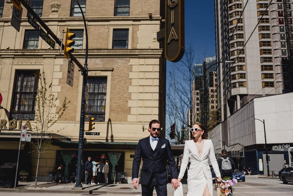 Bride and groom holding hands while crossing at a stoplight.