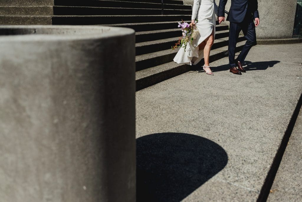 Bride and groom walking down concrete steps, holding hands, with the bride carrying a bouquet.