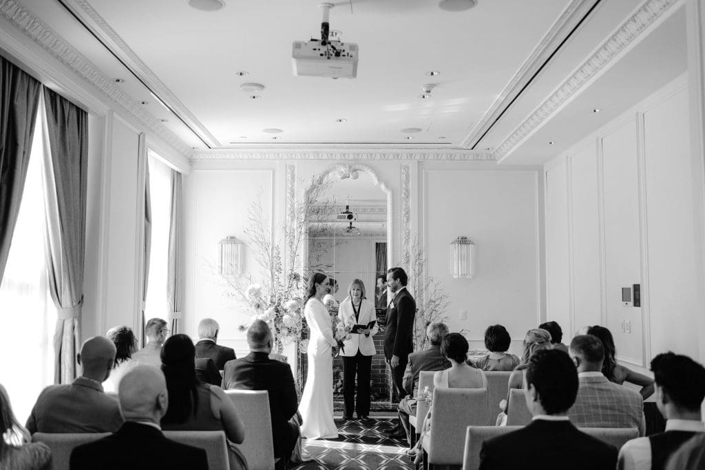 Black and white moment as the bride meets the groom at the altar, witnessed by loved ones.