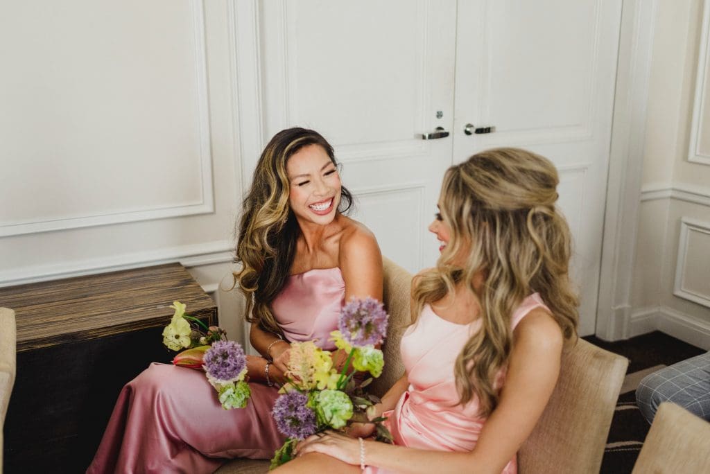 Candid moment of bridesmaids sharing a joyful conversation with smiles.