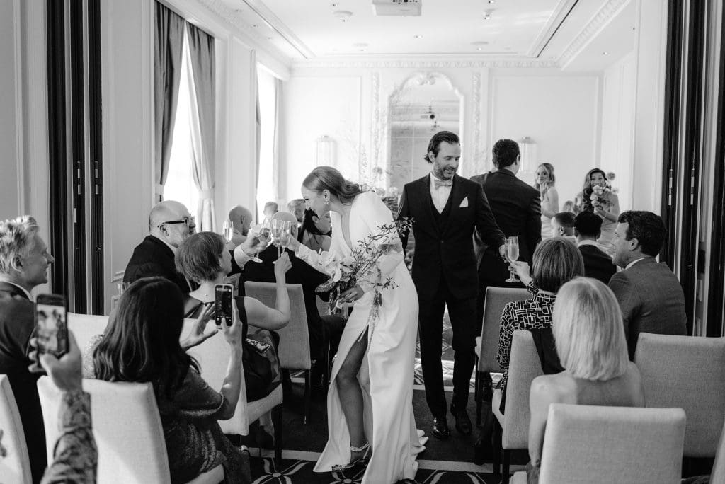 Timeless black and white moment of the bride and groom raising a toast and sharing a joyful cheer with their parents.