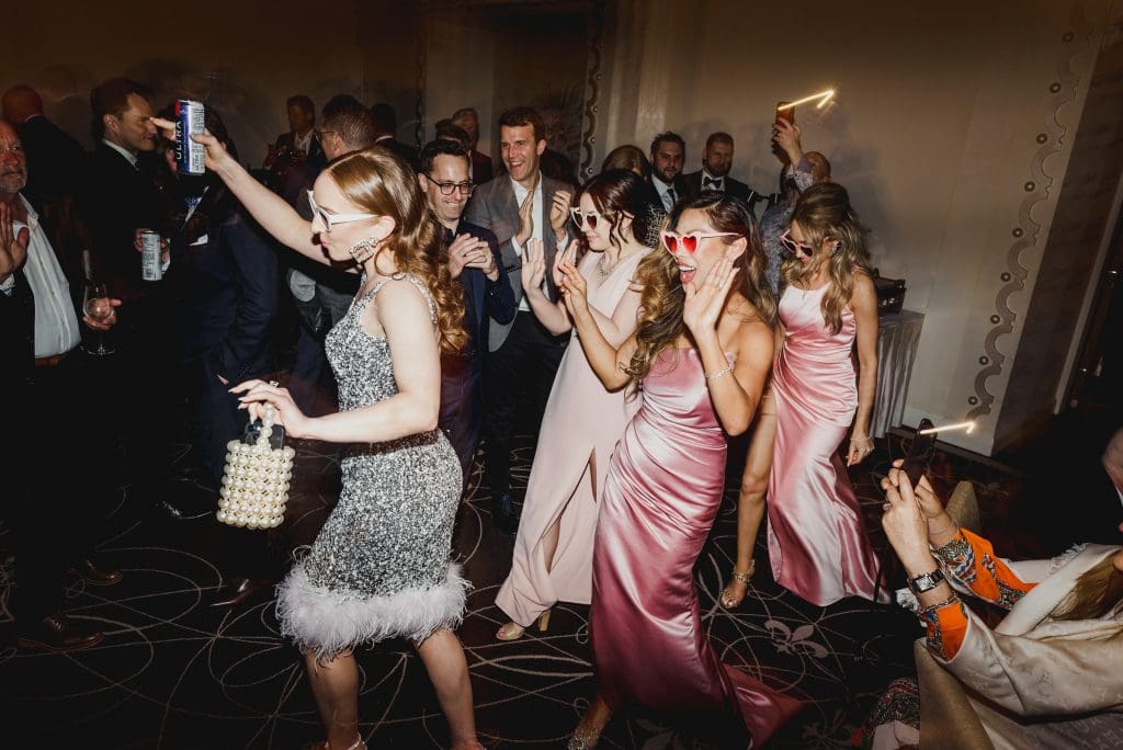 Bride in a silver dress dancing with bridesmaids at the wedding after-party.