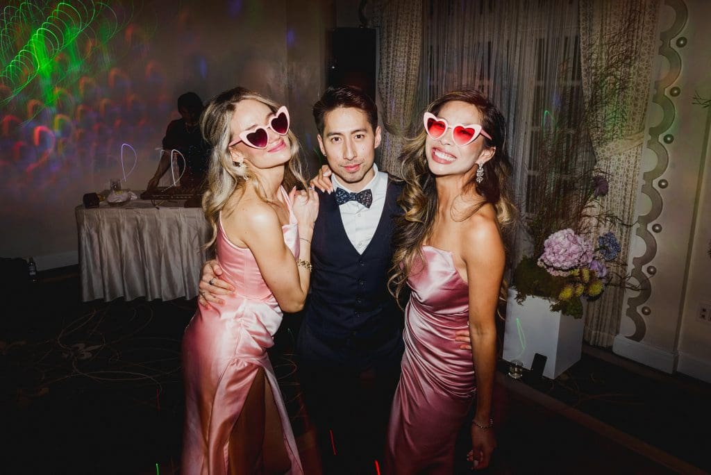 Wedding after-party with two bridesmaids in pink dresses posing with a groomsman.